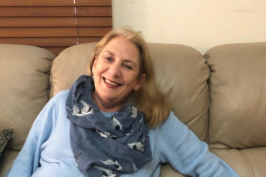 A woman smiles as she sits on a lounge next to a small white and grey dog.