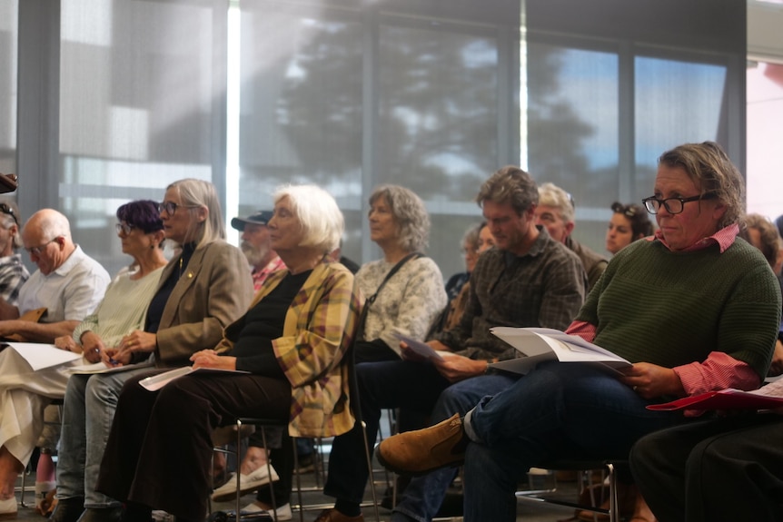 A lagre group of people sit in a community hall.