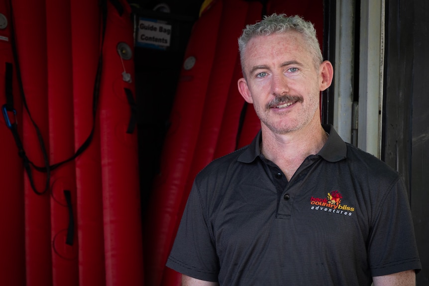 A smiling, grey-haired man with a moustache wears a branded polo shirt.