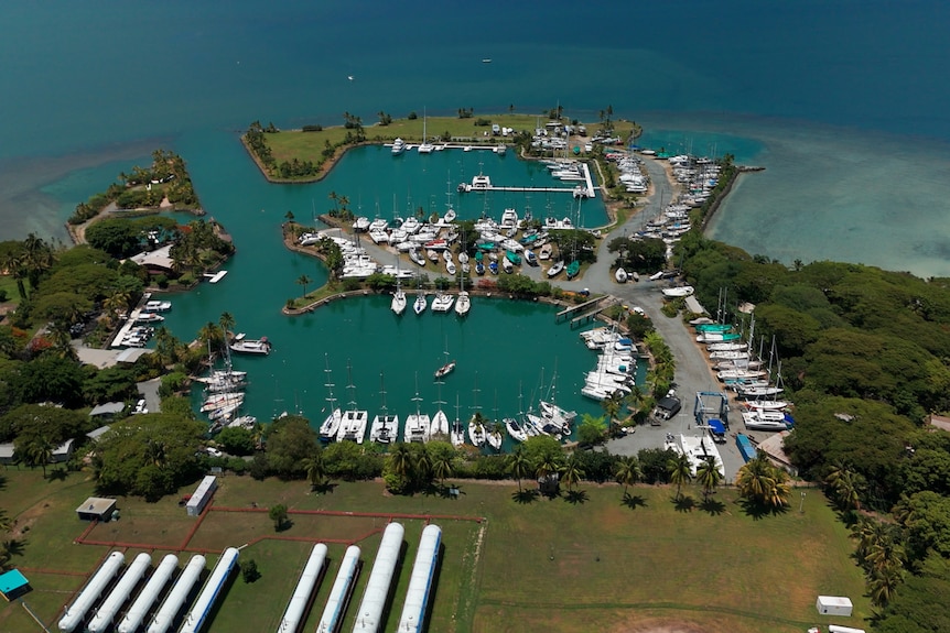 An aerial view of a marina with several boats docked around the inside of a circular harbour.