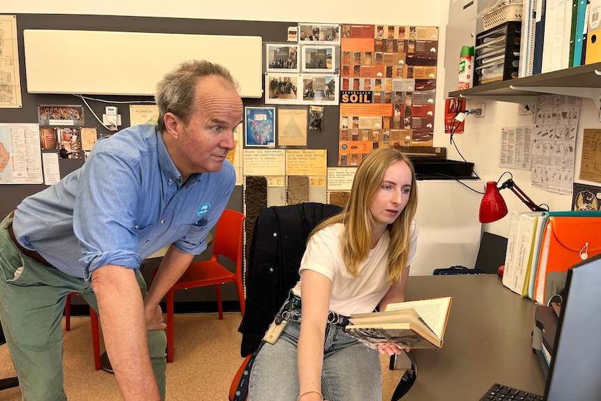 A man and a woman look towards a computer at a desk.