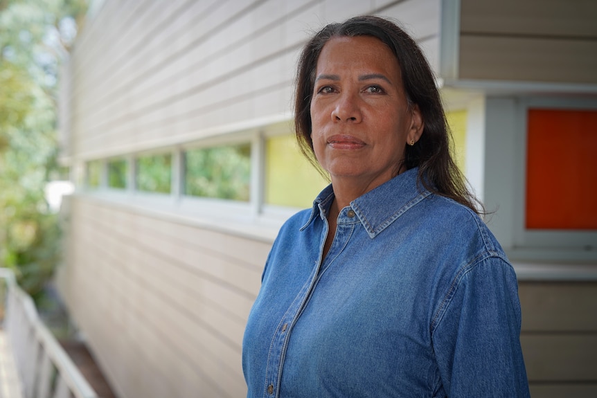 A woman in a denim outfit, wearing a serious facial expression as she looks down the barrel of the camera.