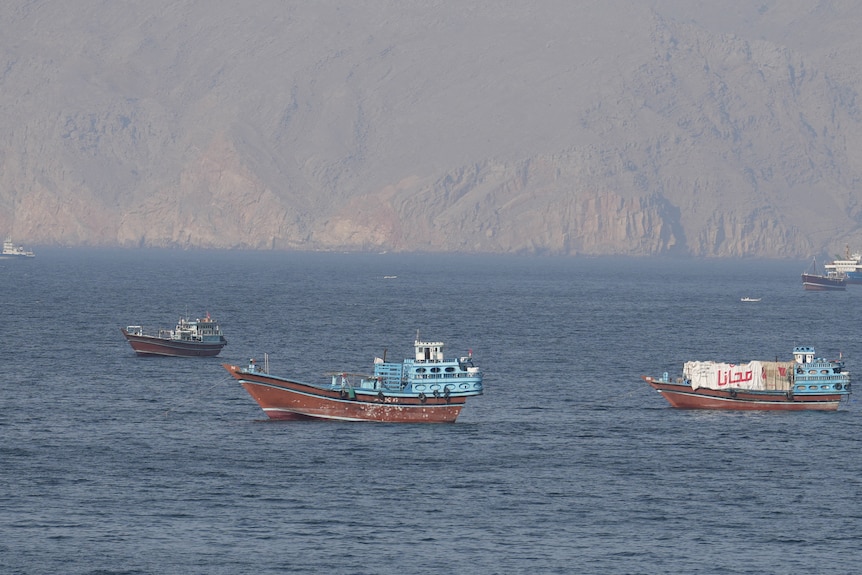 Ships sit still in a body of water with steep, brown cliffs behind them in the distance
