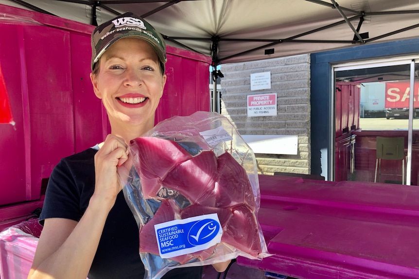 A smiling woman holds up a pack of tuna.
