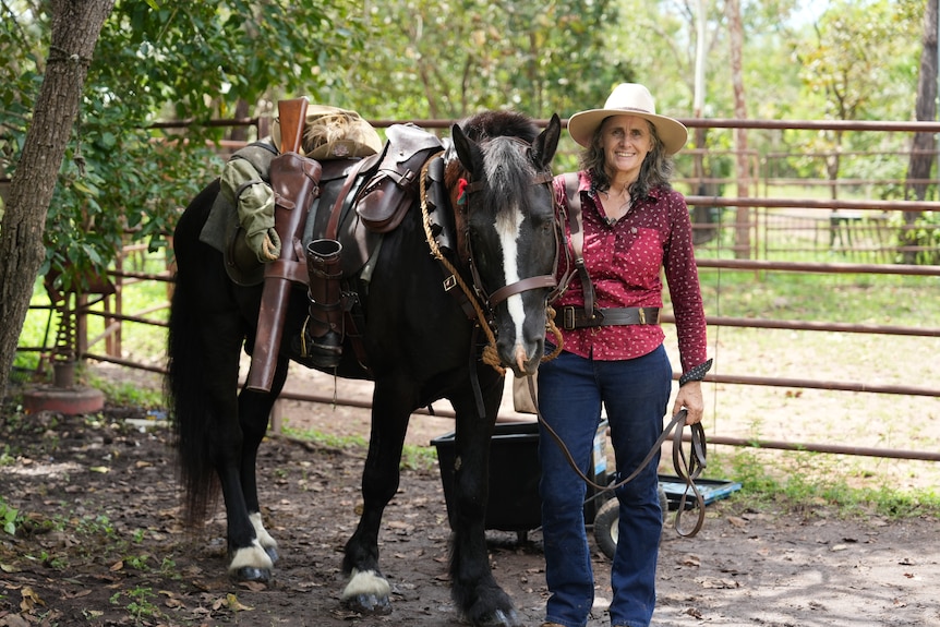A woman, smiling widely, standing next to a horse, with a number of wartime relics attached to its saddle.