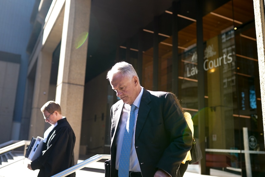 A middle-aged man in a suit walks away from a court with his head looking down.