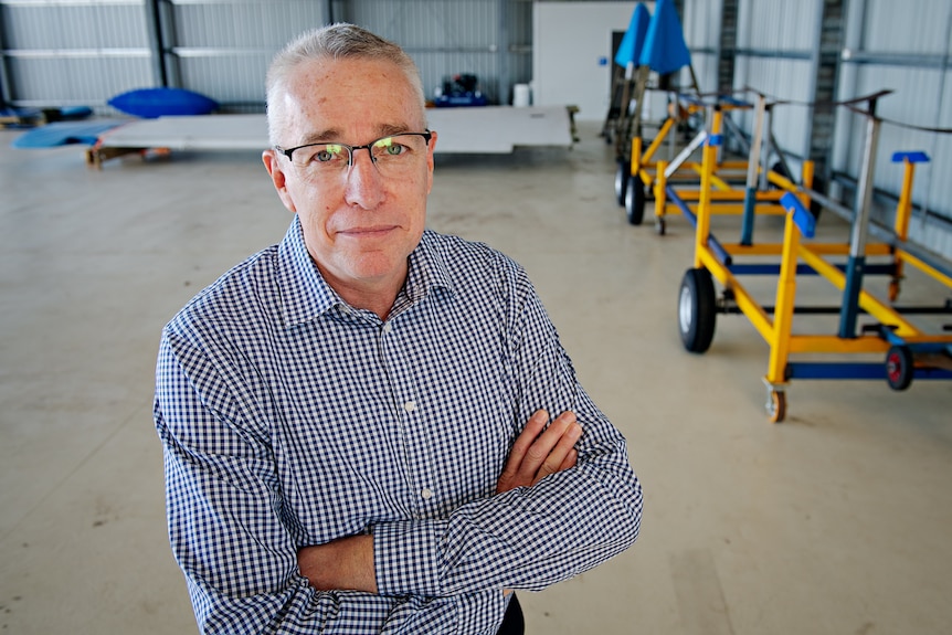A white man in a blue-white checkered button-up shirt, gray short cut hair, glasses, shed inside background