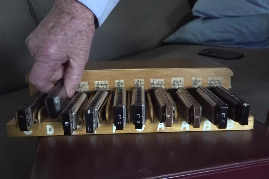 Set of harmonicas with elderly gentleman's hand returning one to the set