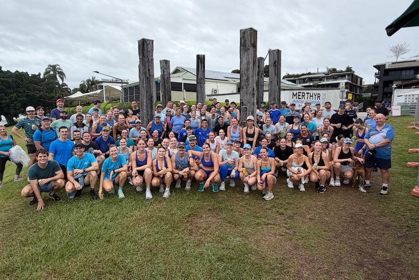 A large crowd of people in workout gear pose for a photoin a park.
