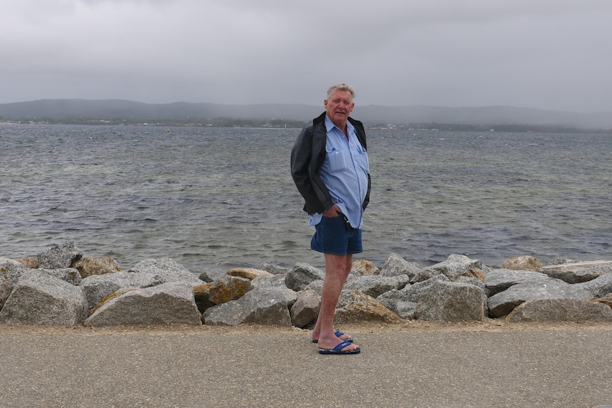 A wide shot of a man standing in front of water on a path at Albany.