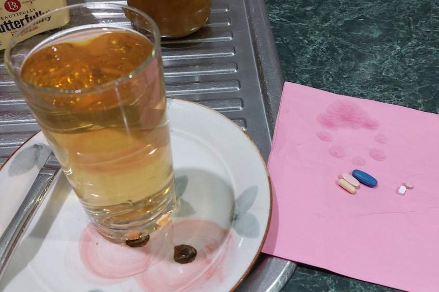 Cup of water with yellow-brown coloured water inside, next to a napkin with pills.