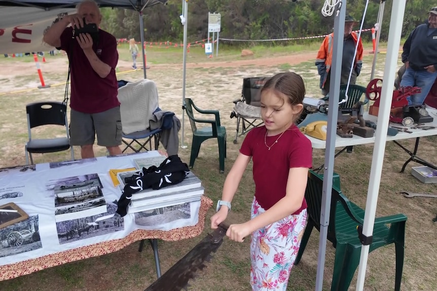 A young girl holds the end of a two man saw
