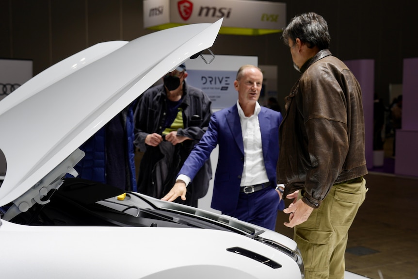 Scott talks to another man next to a white car with its bonnet raised.