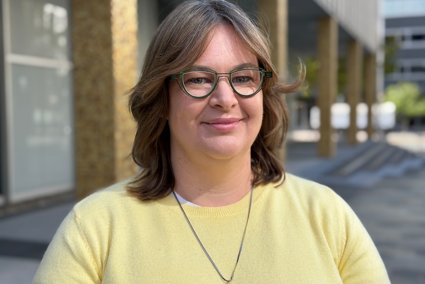 Suzanne Orr wearing a yellow top and black glasses.
