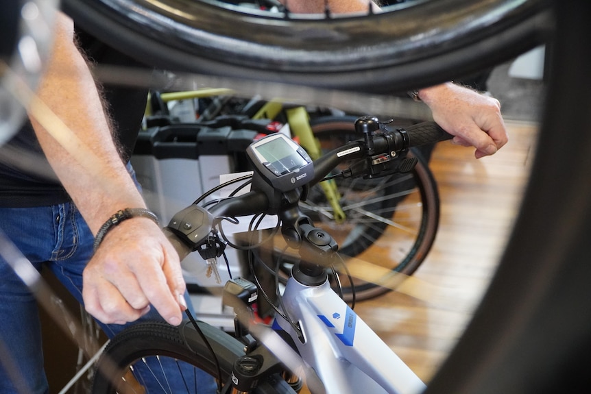 A close-up shot of a man's hands on the handlebars of an electric bike in a cycle shop.