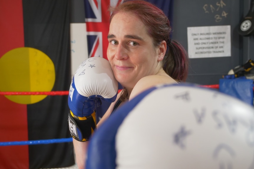 Boxing glove to camera and woman smiling with her other glove to her cheek.