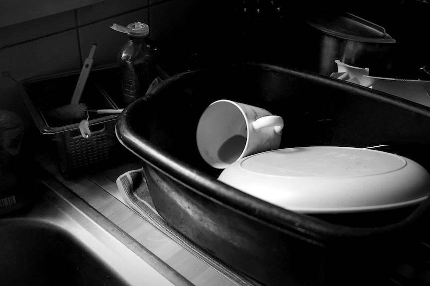 A plate and a cup with leftover tea sits in a large plastic container near the sink.