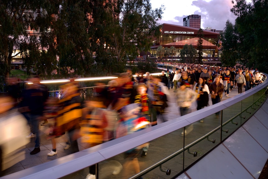 A long exposure blurred shot of a packed crowd crossing a bridge in front of the Adelaide Convention Centre.