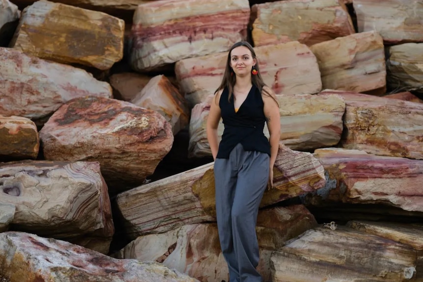 Brooke stands in front of colourful rocks in the bush.