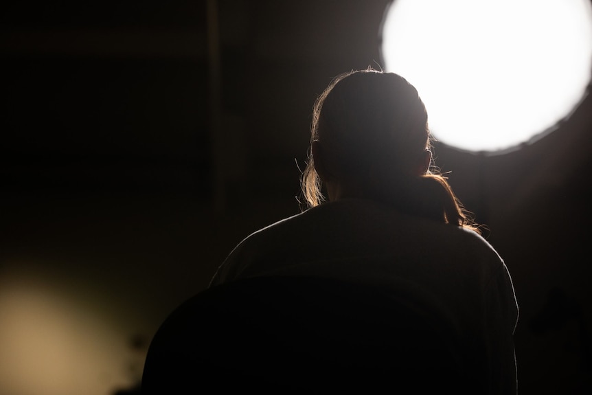 A girl is shown in shadow with a bright light above her 