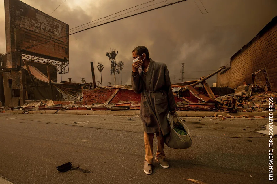 A man walks past a business ruined by fire. The Eaton Fire heavily impacted working-class neighborhoods, where many underinsured homeowners now face gentrification and displacement