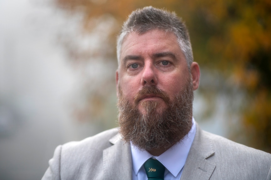 Man with beard and short hair wearing a suit and tie looking serious. 
