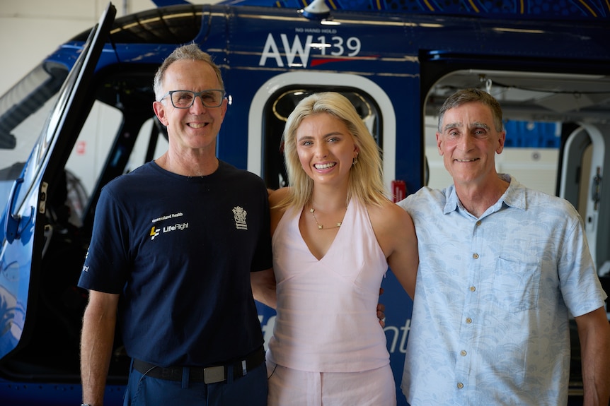 A smiling woman stands between two men in front of a helicopter
