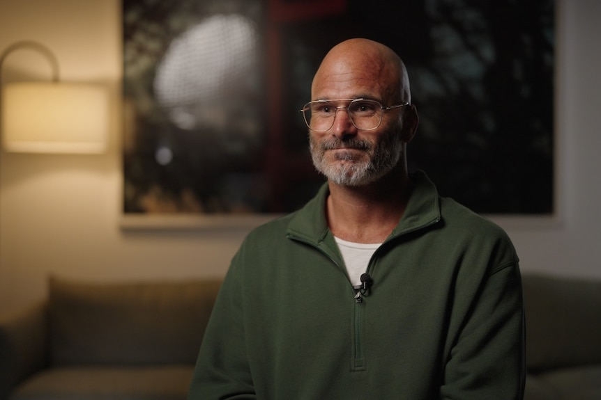 portrait of man with grey hair and glasses in a green jumper
