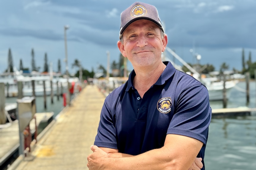 A man with crossed arms looks content as he stands on a wharf at Mooloolaba.