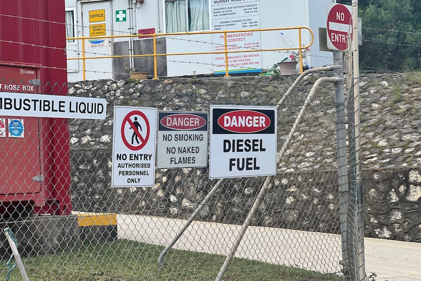 Signs attached to a fence warning about the danger of fuel on premises.