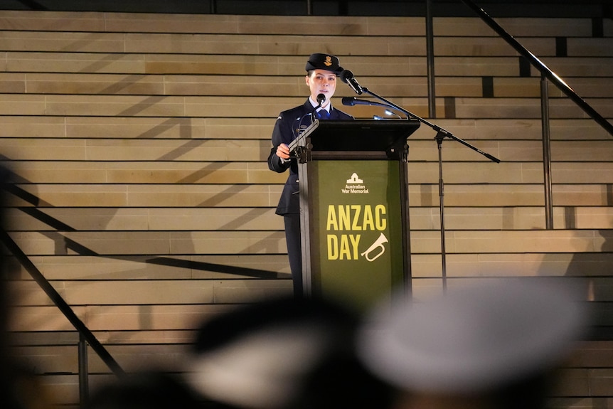 A woman stands behind a lectern speaking while in uniform.