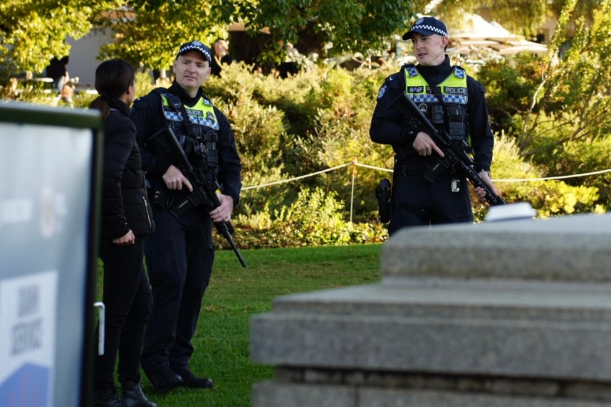 Two uniformed police officers carrying large firearms, talking to an unidentified person, in Kings Park.