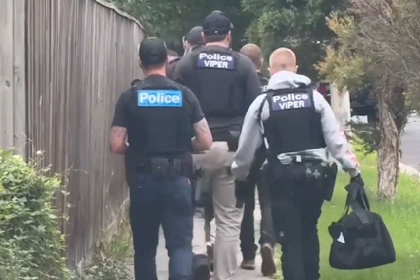 Rear view of several police officers walking in a row along a pavement.