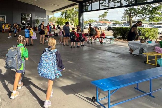 A wide shot of a school multi-purpose building with students and families gathered around market stalls
