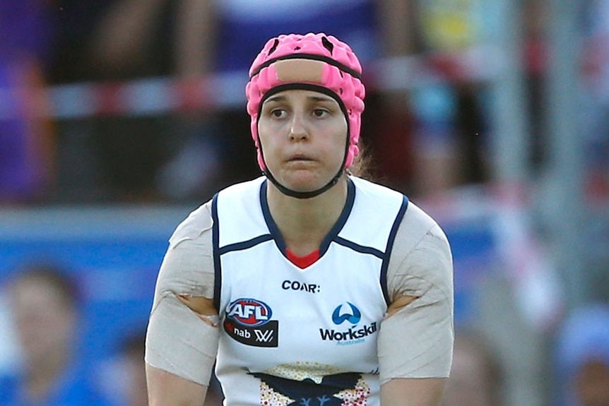 A female AFL player lines up a kick.