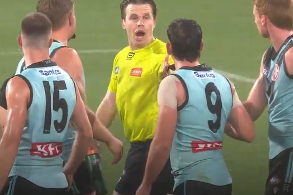 an afl umpire in hi-vis yellow top speaks to player in aqua guernsey with back displaying teh number 9