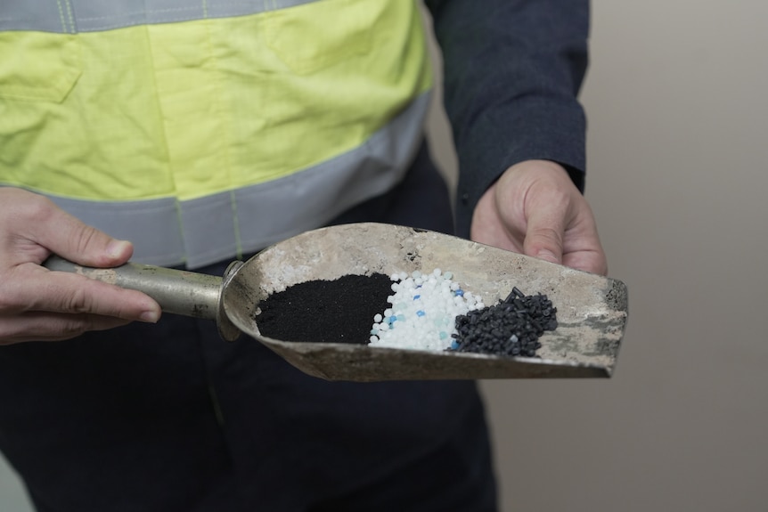 A researcher grasping a small steel scoop, showing the three different types of recycled material pellets it holds.