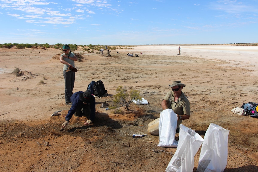 Three people working on plain dirt ground digging a hole