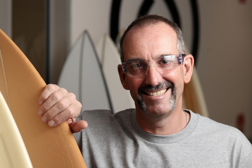 Man wearing lab protective eyewear, smiling in front of surfboards