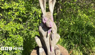 A wooden hare with pink paint splashed on its eyes, nose and paws.