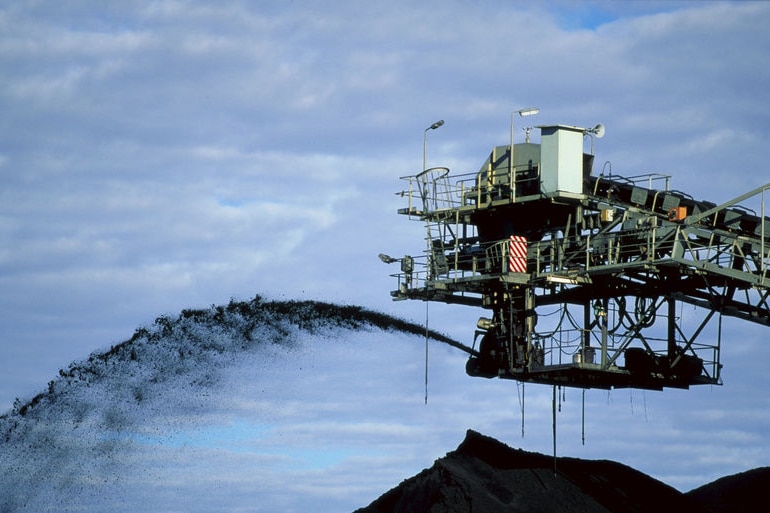 A mine conveyor belt sprays coal in the air into a pile dug from a mine.
