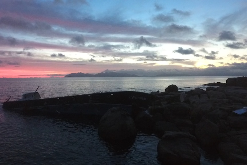 A boat stuck on rocks framed by a sunrise