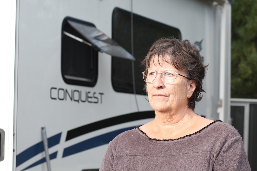 A woman with short hair stands in front of her caravan.