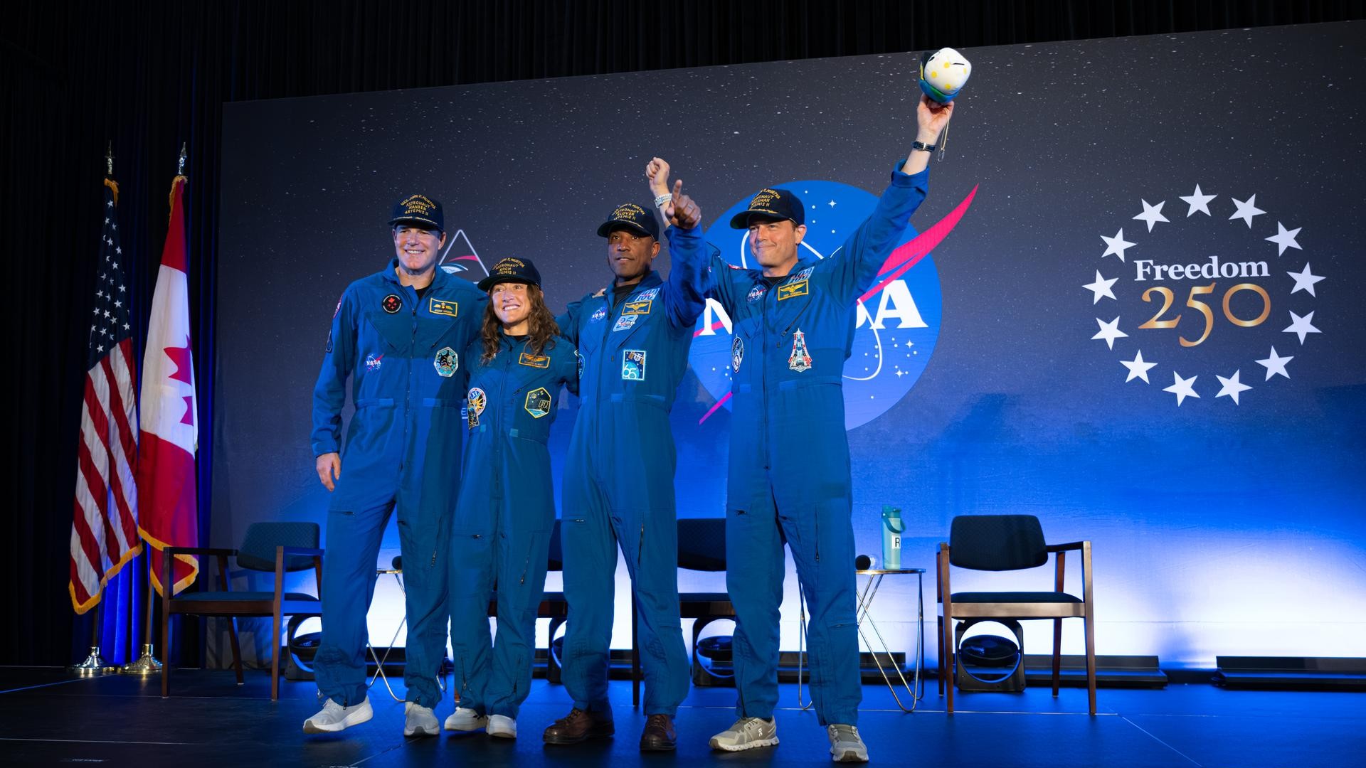 a man in an orange flight suit smiles while carrying a small stuffed moon