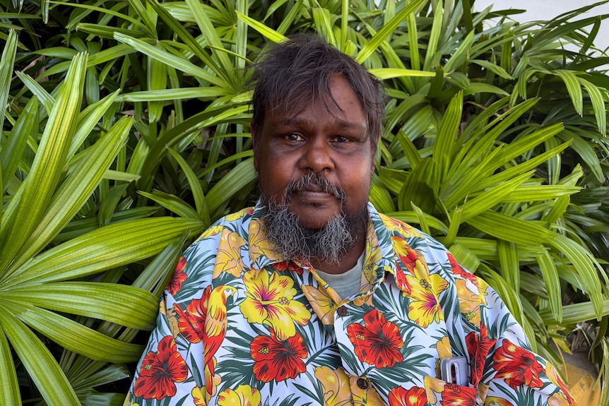 Man in floral shirt stands in front of green plants