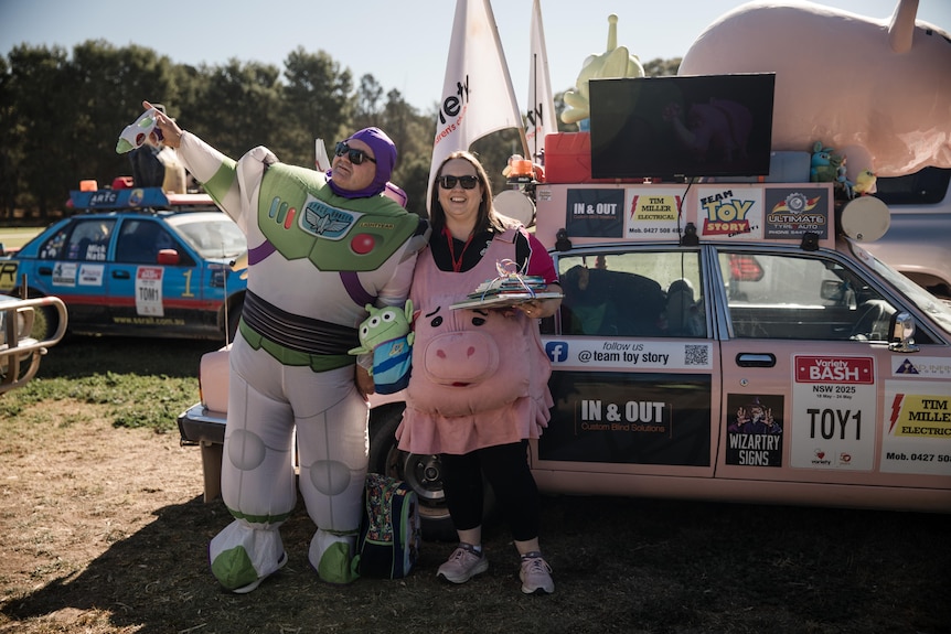 Two people dressed as characters from Toy Story standing in front of a car.