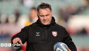 Trevor Woodman holds a rugby ball under his left arm to his chest while holding his right arm out and pointing his index finger during a pre-game warm-up