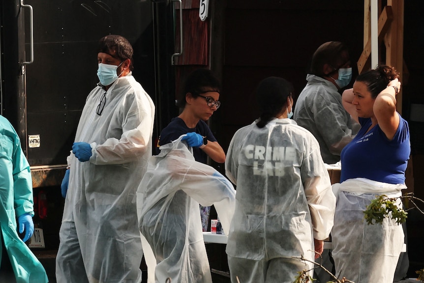 Crime scene investigators putting on full-body PPE out the front of a home.