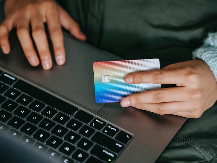 One hand on a laptop's trackpad while another hand holds a credit card.