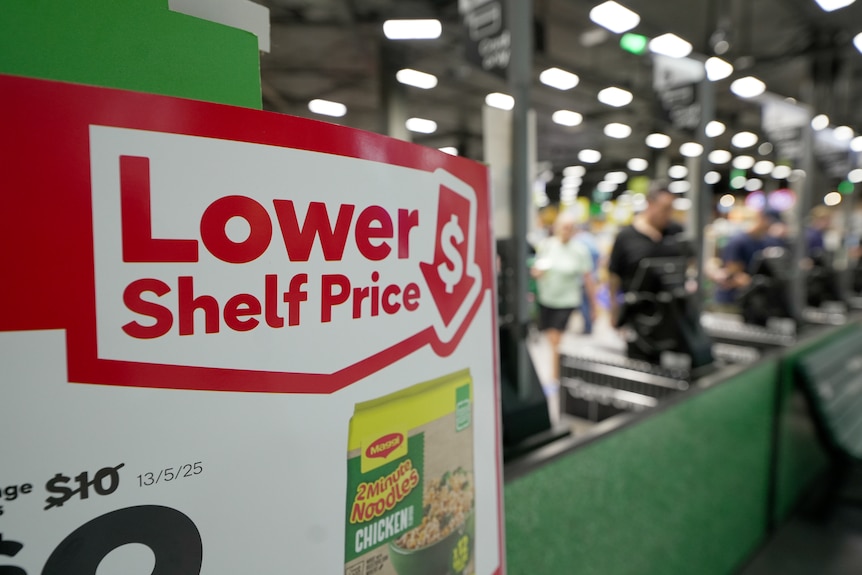 Close up of a lower shelf price sign with registers in the background inside a Woolworths store.